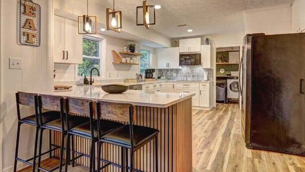 A kitchen with a central island, bar stools, pendant lights, and a refrigerator. - Luxury 3BR Getaway 2 Master Suites Pool & More, Great Location (Stone Mountain)