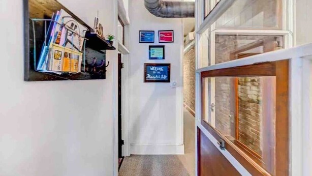 A hallway with a bookshelf, framed signs, and a door leading to a room with a brick wall. - The Honesdale Loft - downtown historic Main St (Honesdale)