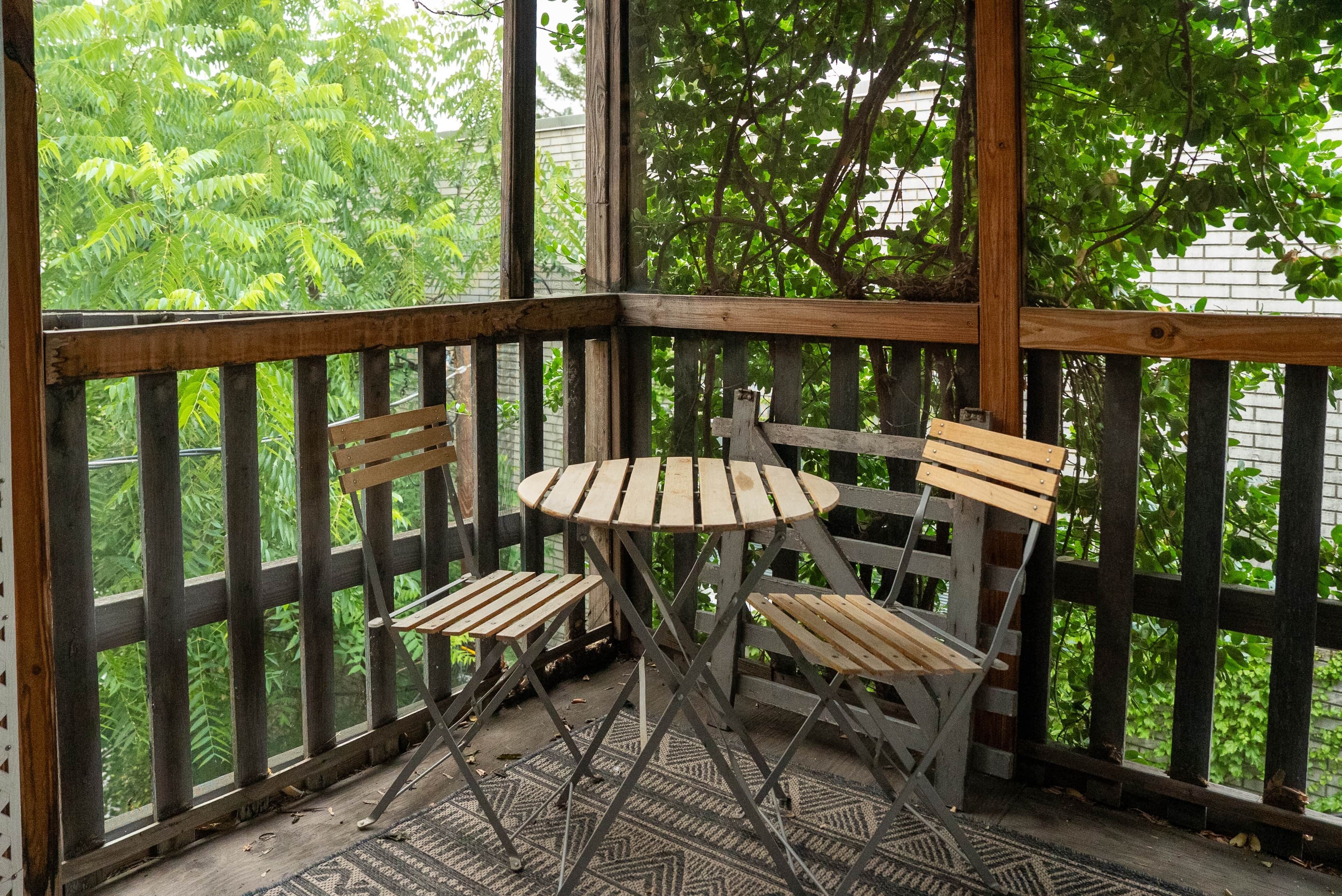 Eine Holzterrasse mit Tisch und zwei Stühlen, umgeben von einem Metallgeländer.
