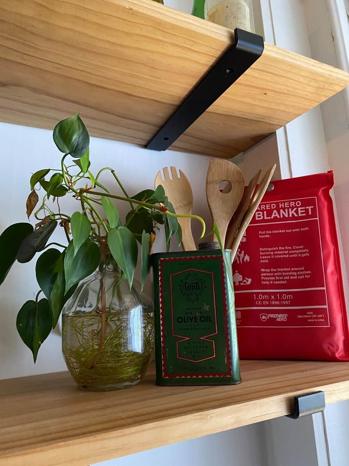 Een plank met een fles groene olijfolie, een rode branddeken, houten keukengerei en een potplant.