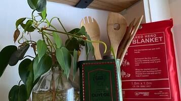 Een plank met een fles groene olijfolie, een rode branddeken, houten keukengerei en een potplant.