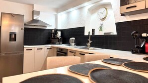 Une cuisine moderne avec un réfrigérateur en acier inoxydable, un dosseret de carrelage noir et une horloge au mur.
