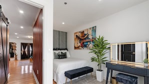 A bedroom with a bed, a desk with a mirror, a large abstract painting, and a potted plant. - Best Location! Walk to Broadway & Downtown! Balcony-2 Car Parking-Laundry-Wi-fi (Nashville)