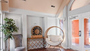 A room with a red brick floor, a white chair, a potted plant, a wall clock, and a door leading to a brick exterior. - Best Location! Walk to Broadway & Downtown! Balcony-2 Car Parking-Laundry-Wi-fi (Nashville)