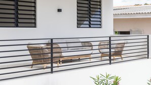 Ein Balkon mit weißem Geländer, einer Couch und zwei Korbstühlen.