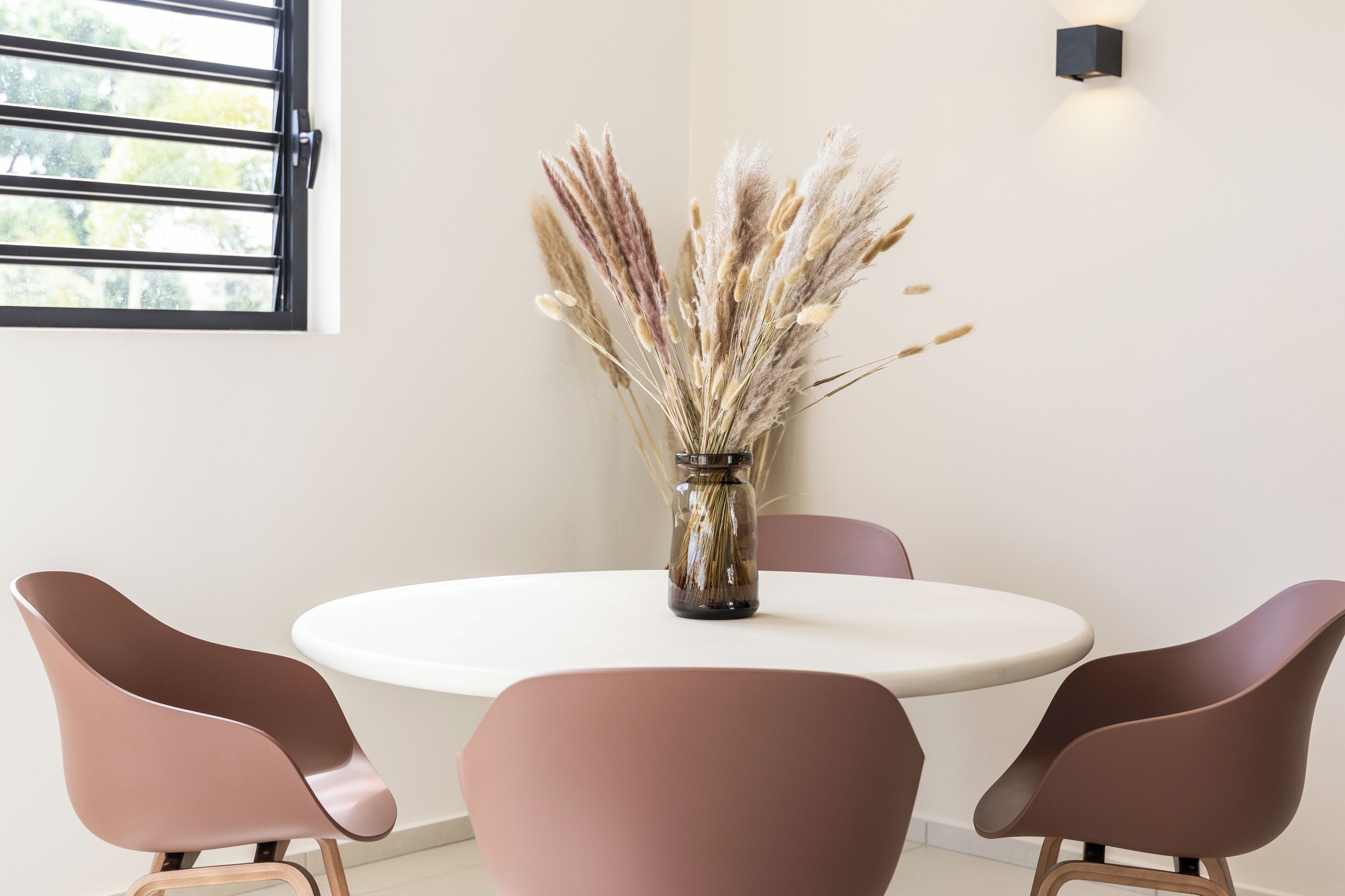 A round table with a vase of pampas grass, surrounded by four chairs. - Vista Mar Curaçao (Jan Thiel)