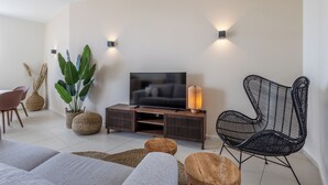 Ein modernes Wohnzimmer mit einem Flachbildfernseher, einem schwarzen Gewebesessel und einem Holztischchen.