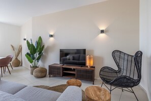 A modern living room with a flat-screen TV, a black woven chair, and a wooden console table. - Vista Mar Curaçao (Jan Thiel)