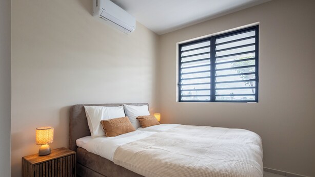 Ein Schlafzimmer mit Bett, Nachttischlampen, einem Fenster und einer Klimaanlage.