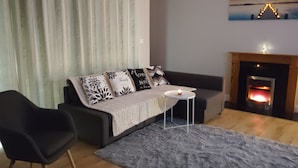Una sala de estar con un sofá, una mesita redonda, una silla, una chimenea y un cuadro en la pared.