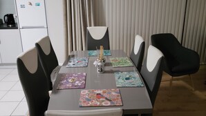 A dining area with a table set for four, surrounded by chairs with white cushions. - 2 Bedroom Apartment 4-6 People-coastal Comfort (Balbriggan)