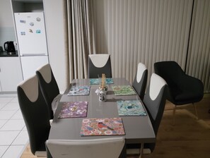 A dining area with a table set for four, surrounded by chairs with white cushions. - 2 Bedroom Apartment 4-6 People-coastal Comfort (Balbriggan)