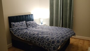A bed with a dark headboard, a patterned bedspread, and a nightstand with a lamp. - 2 Bedroom Apartment 4-6 People-coastal Comfort (Balbriggan)