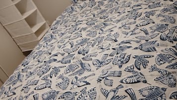 A bed with a blue and white patterned duvet and pillows, a dark headboard, and a white shelving unit to the left.