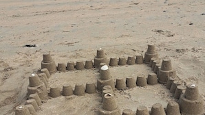 Una playa arenosa con una gran escultura de arena con forma de rostro.