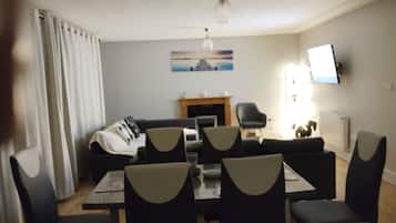 A living room with a fireplace, a television mounted on the wall, and a dining area with a table and chairs.