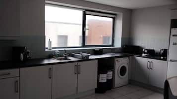 A compact kitchen with white cabinets, a built-in washing machine, and a window providing natural light.