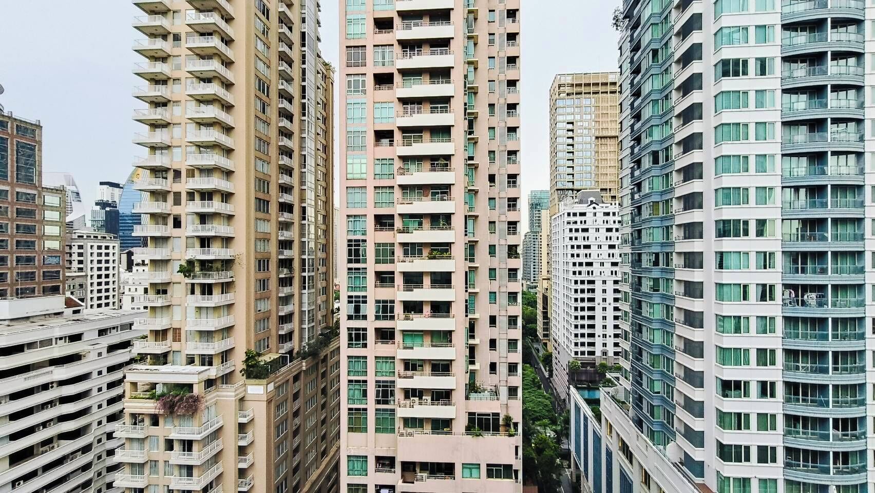 A high-rise residential building with multiple balconies, a modern architectural design, and a dense urban setting.
