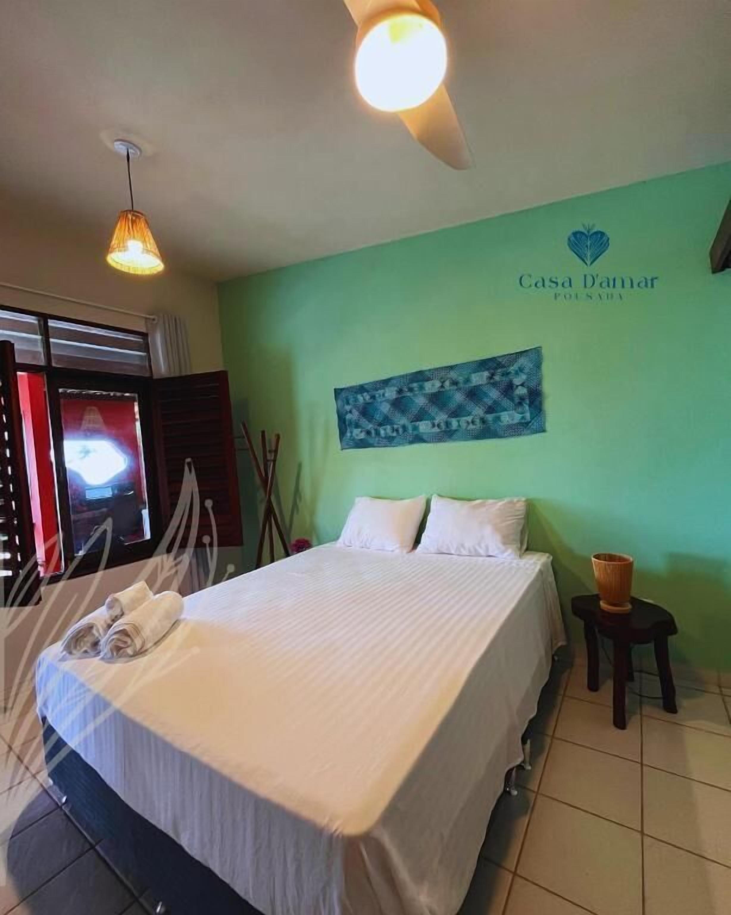 Una habitación de hotel con una cama, una obra de arte colgada en la pared, un ventilador de techo y una mesita con una cesta.