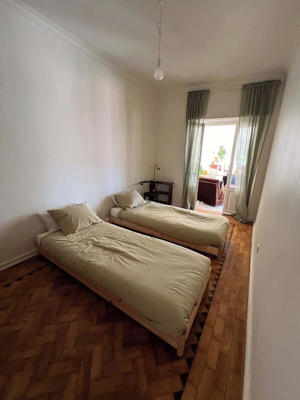 A room with two single beds, a wooden herringbone floor, a desk with a chair, and a hanging light fixture. - Big apt 4beds with terrace, 15 mins to Lisbon (Almada)