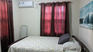 Een slaapkamer met een bed, een kussen, een schilderij en gordijnen.
