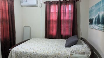 Un dormitorio con una cama, un cojín, un cuadro y cortinas.