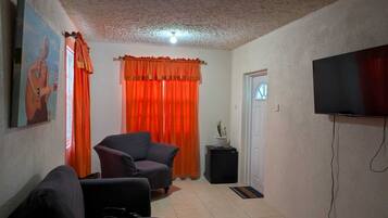 Un salón con un sillón negro, un sofá, un cuadro en la pared, un televisor montado y una puerta con ventanal.
