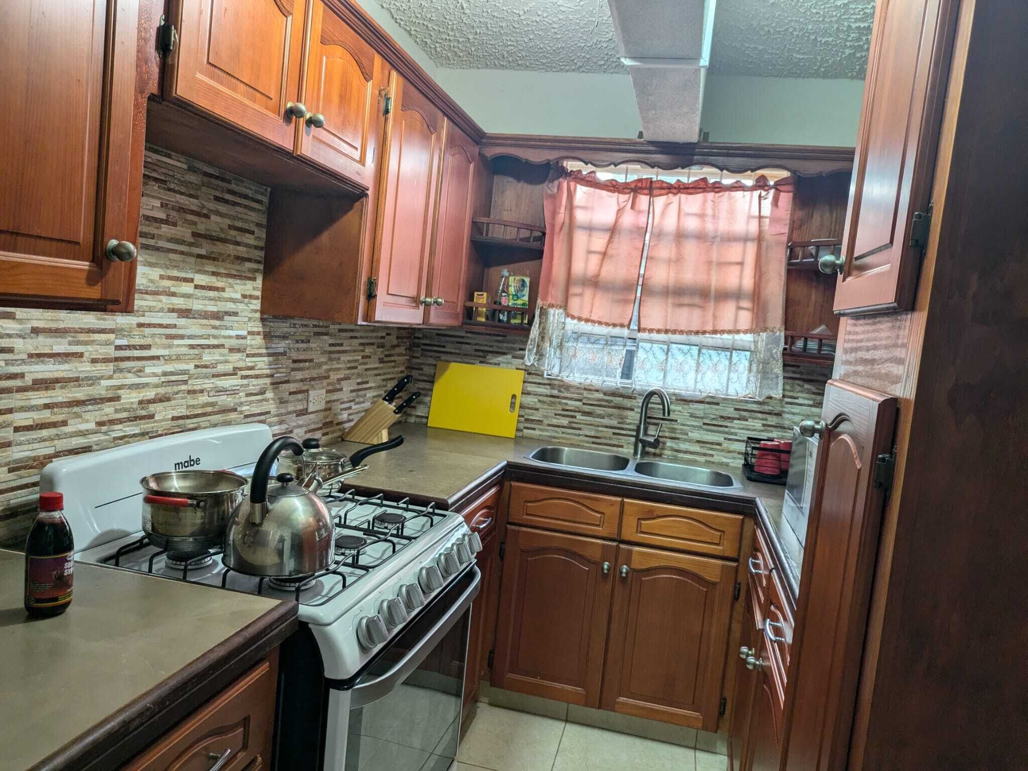 Una cocina con armarios de madera, una estufa a gas, un fregadero y una ventana con cortina.