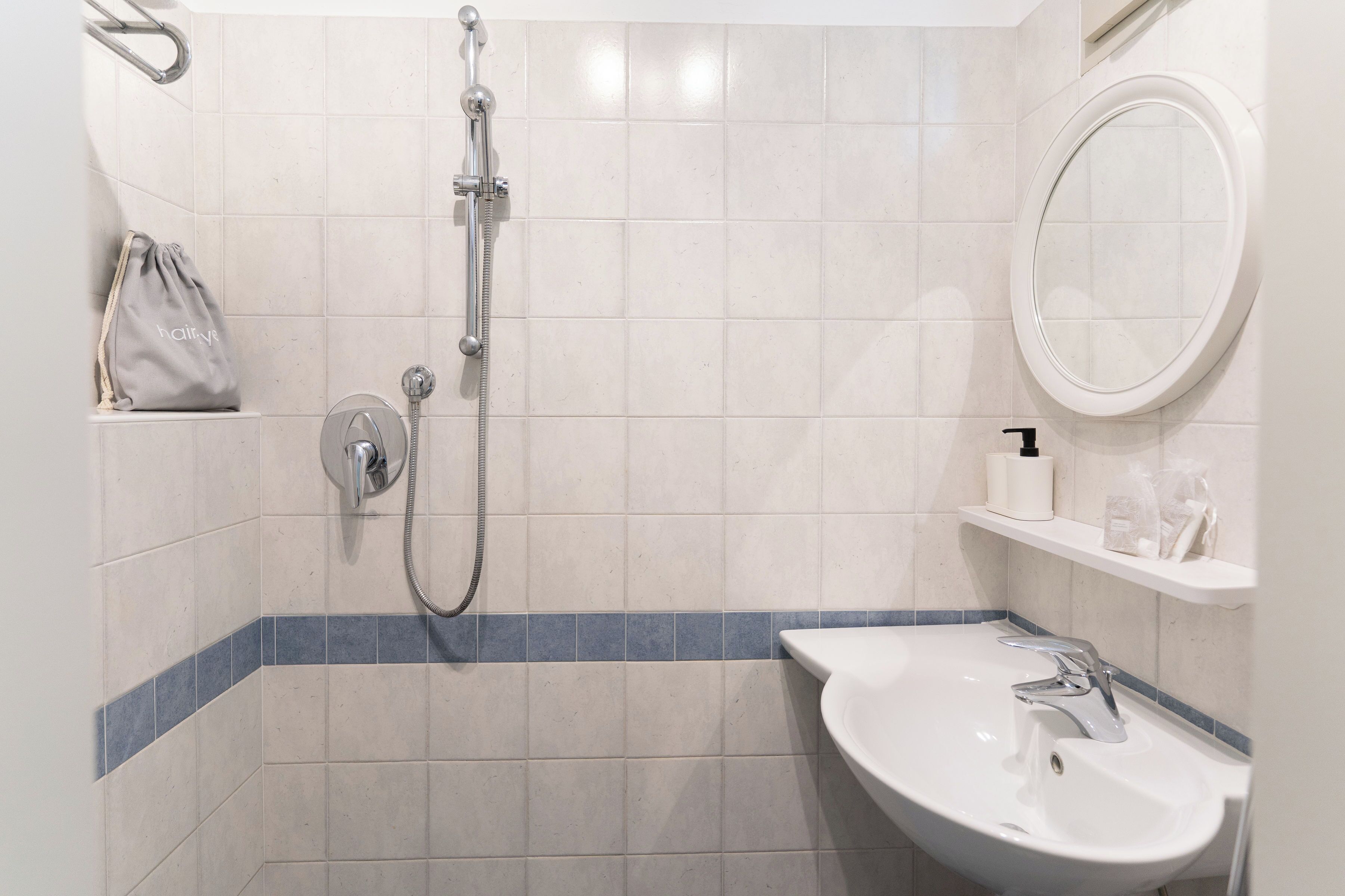 A bathroom with a shower, sink, mirror, and towel rack.
