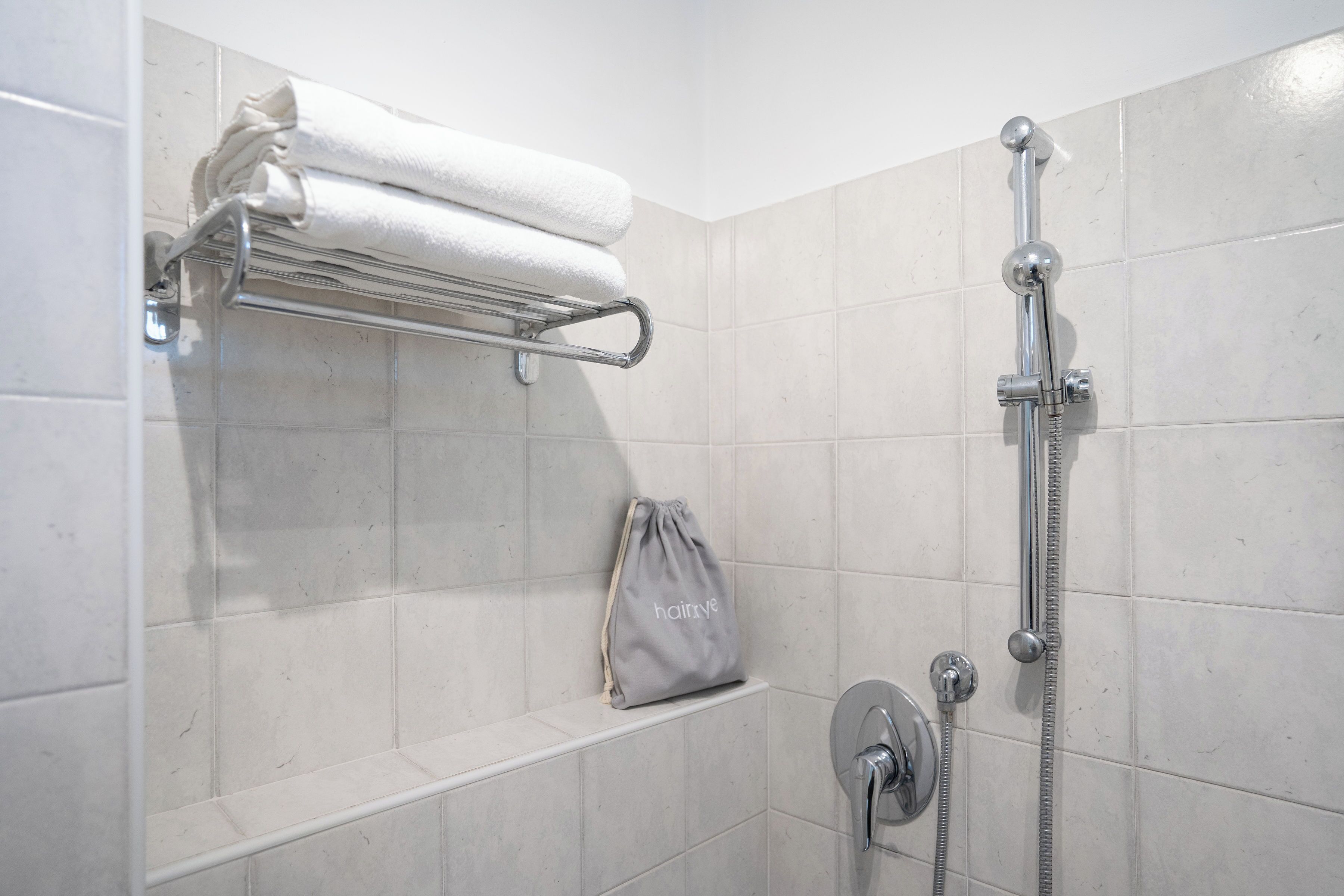 A shower with a handheld showerhead, a towel rack with folded towels, and a small shelf with a bag.