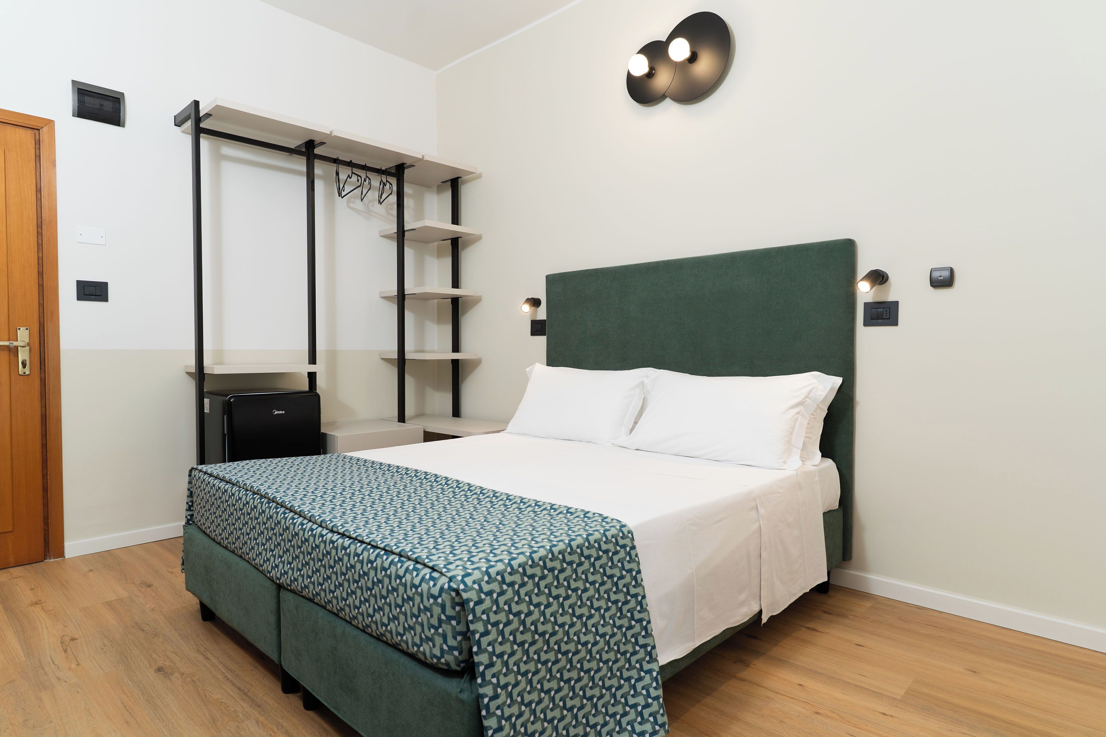 Een slaapkamer met een bed, een kledingkast, een bureau en een wandplank.