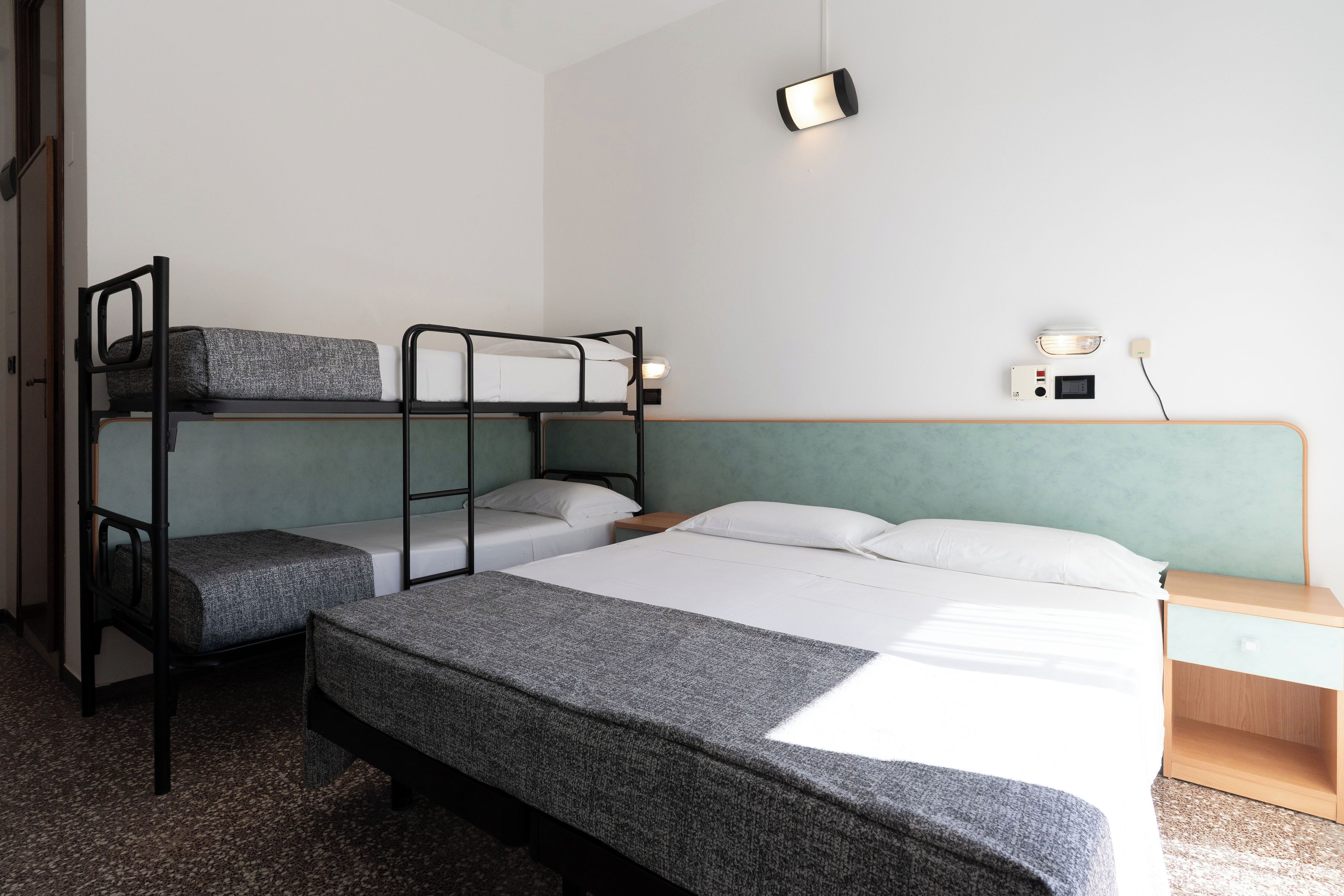 Habitación con literas, un escritorio y mesita de noche, una lámpara fijada a la pared y un enchufe.