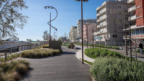 En moderne bysti med en træpromenade, metallygter og en bygning med teksten 'HOTEL SAN FRANCISCO SPAAGIA'.