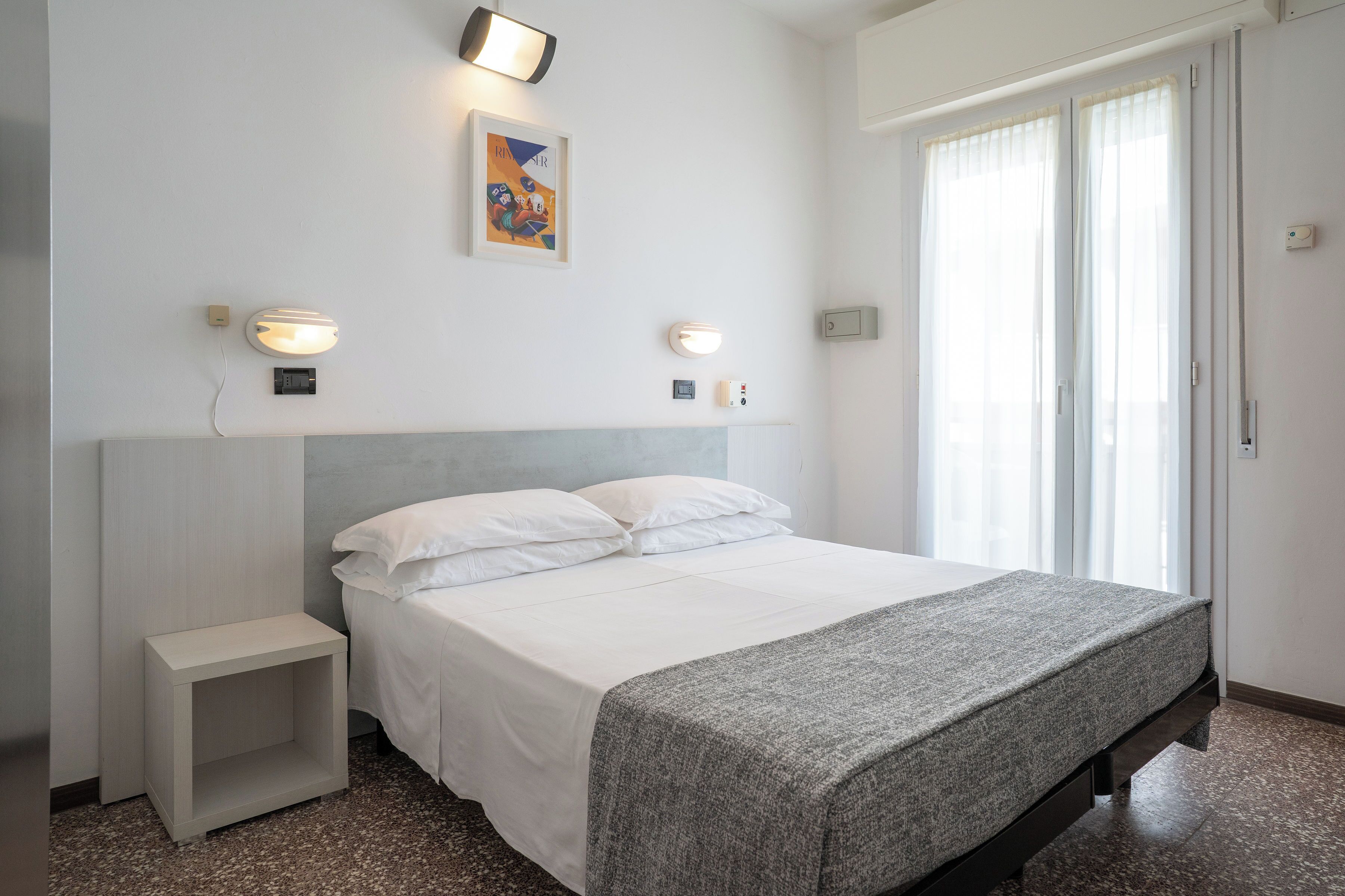 A bedroom with a bed, bedside tables, wall-mounted lights, and a window with curtains.