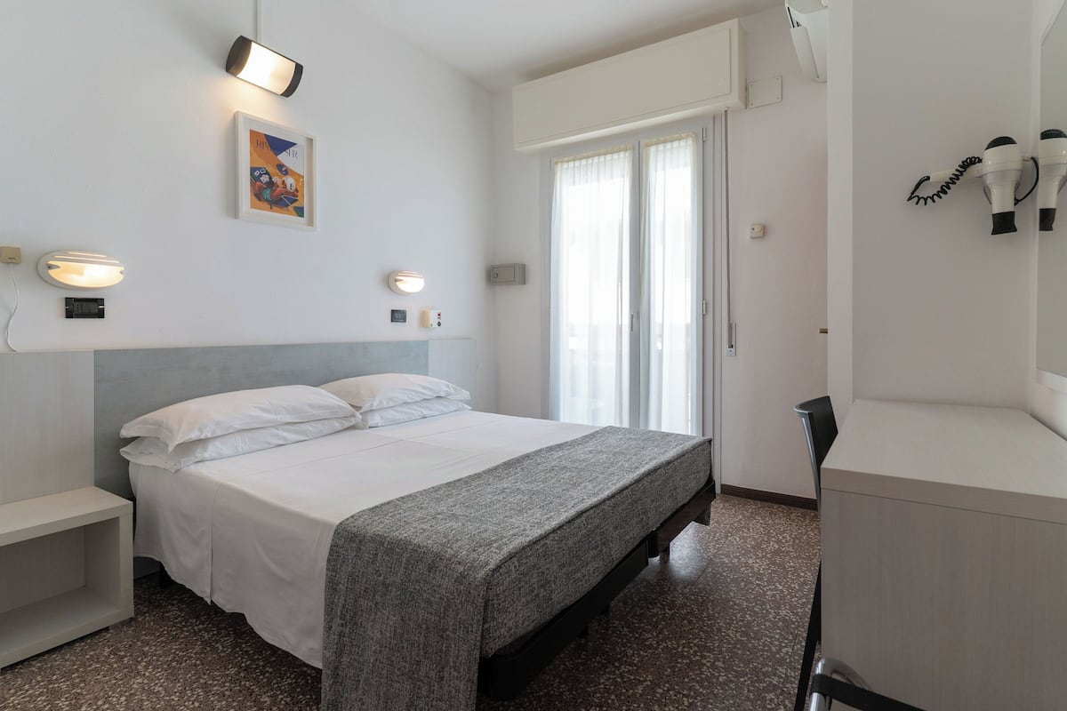 A hotel room with a bed, bedside tables, a desk, and a window with curtains.