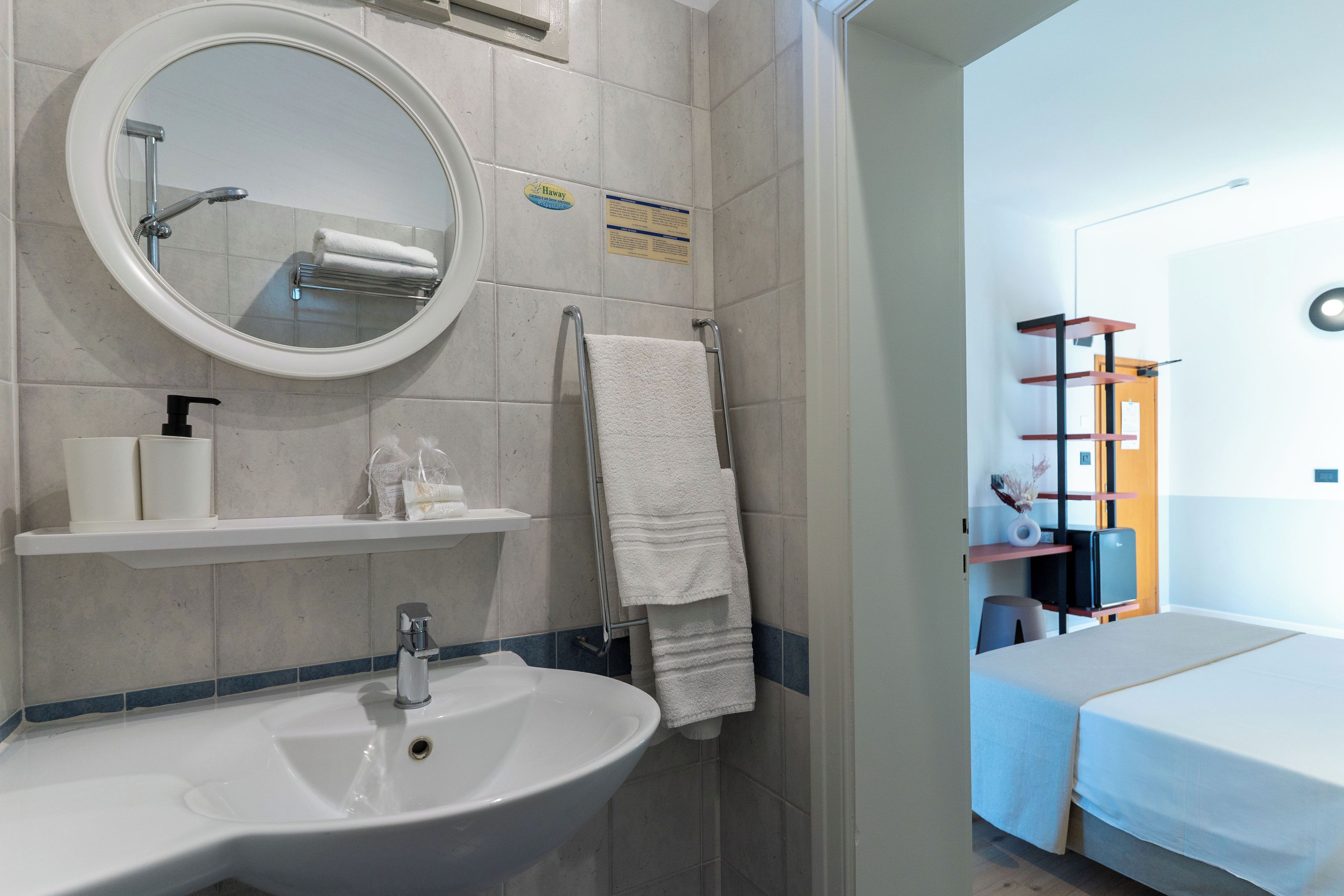 A bathroom with a sink, mirror, towel rack, and a sign on the wall.