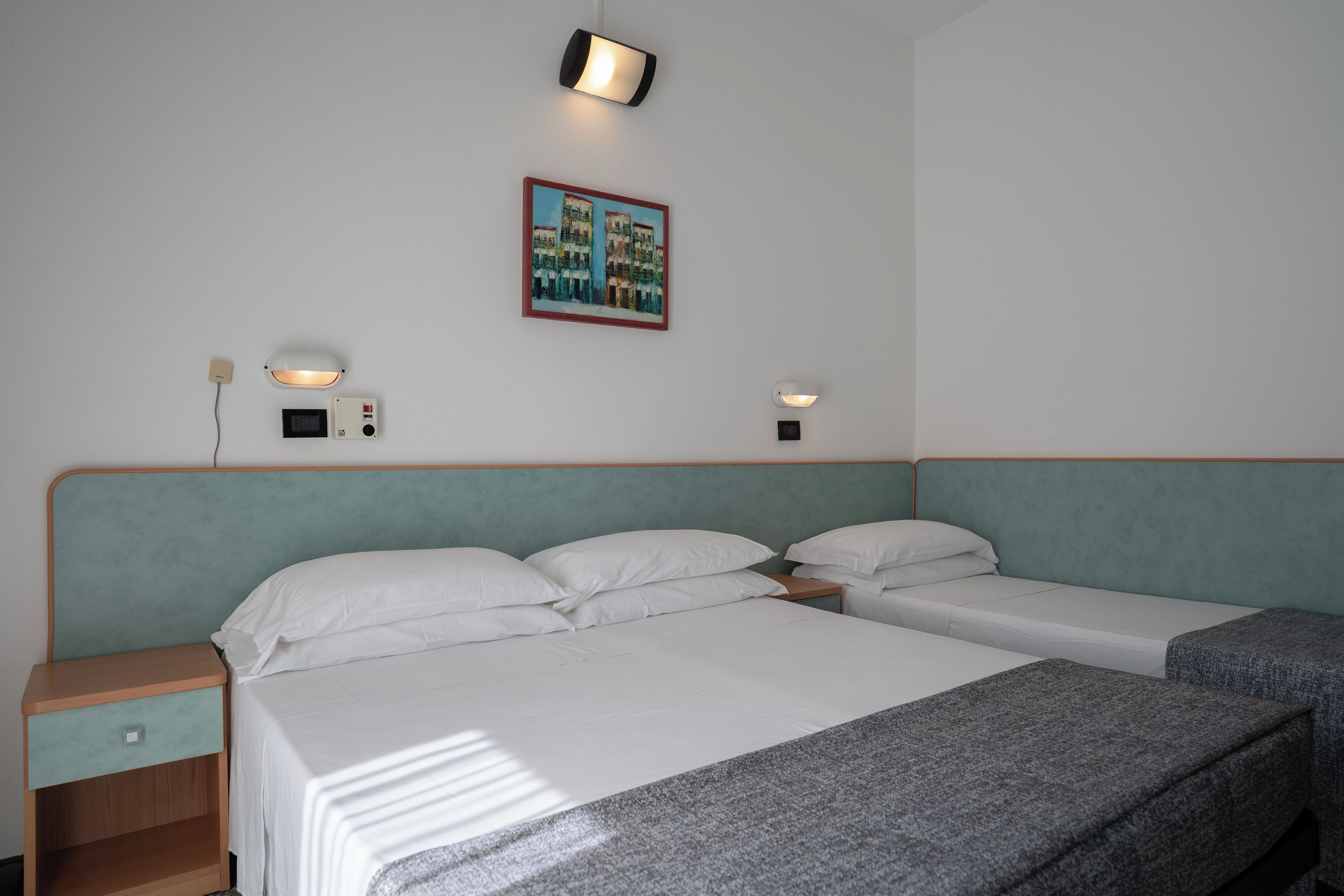 A hotel room with two beds, a nightstand, a wall-mounted light, and a framed picture.