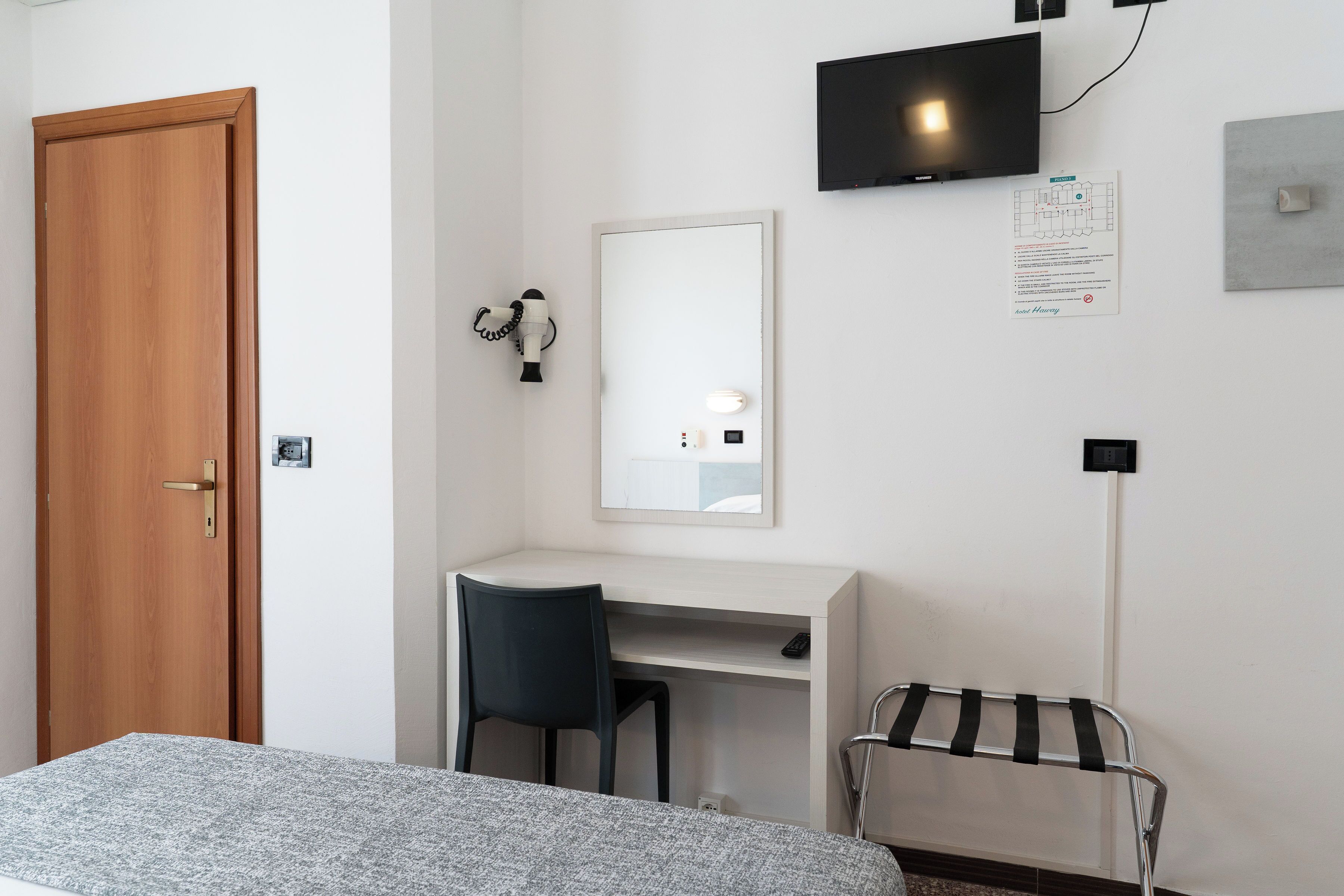 A room with a bed, a desk, a chair, a TV, a mirror, and a hairdryer.