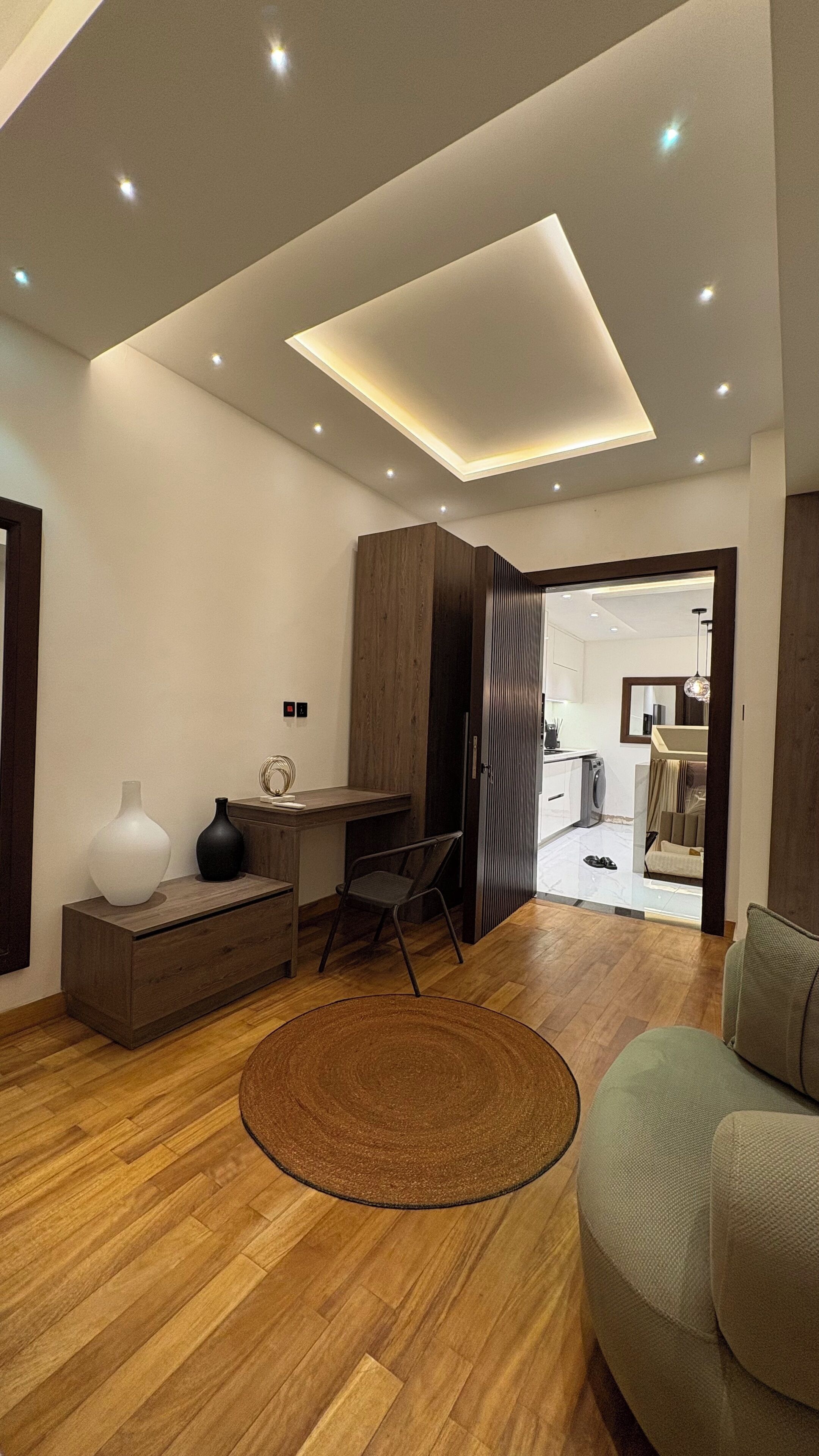 A modern living room with a wooden floor, a round rug, a sofa, a desk, and a cabinet.
