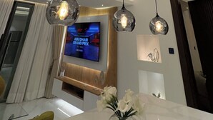 Ένα μοντέρνο σαλόνι με ψηλό ταβάνι, εντοιχισμένο φωτισμό, μια τηλεόραση τοποθετημένη στον τοίχο και μια τραπεζαρία με ένα τραπέζι από μάρμαρο.