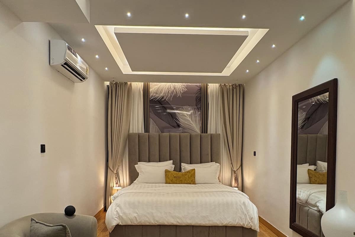 Un dormitorio moderno con una cama grande, un tapete redondo, una silla y un espejo.