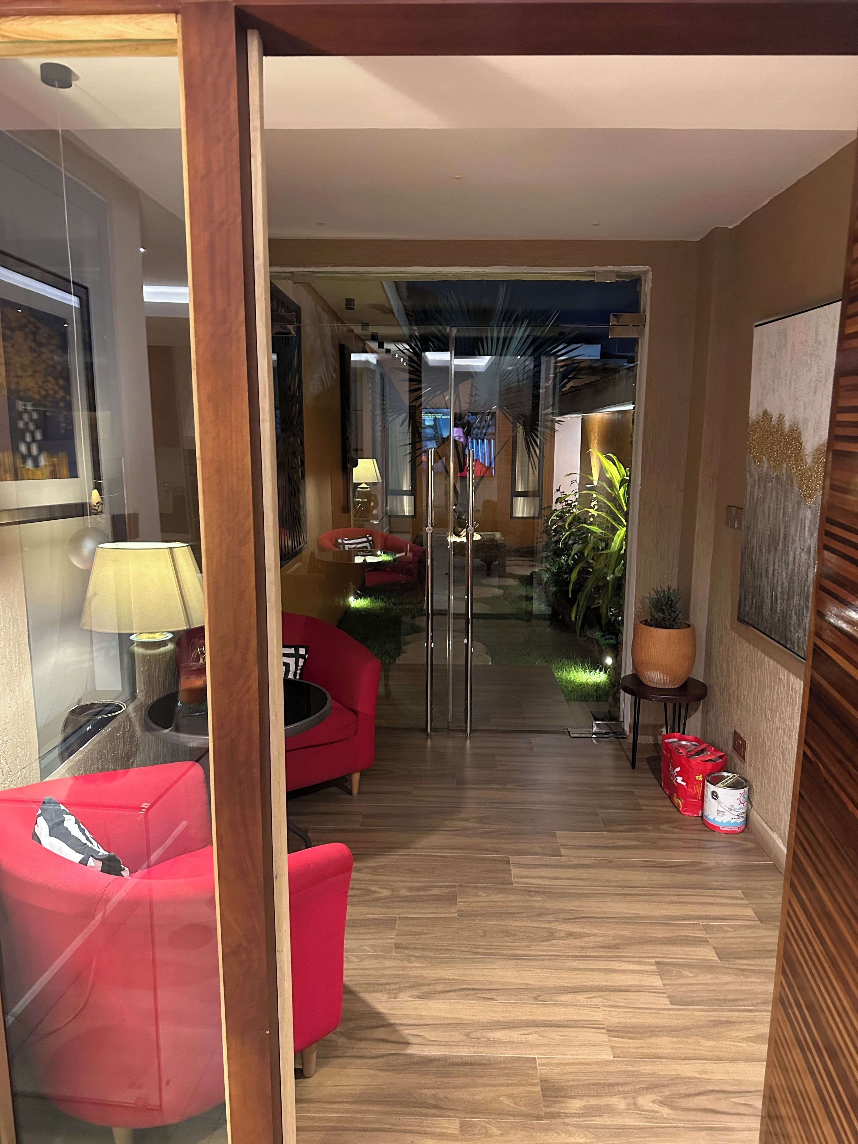 A modern interior with a wooden floor, red sofas, a glass partition, and a small garden area visible through the partition.
