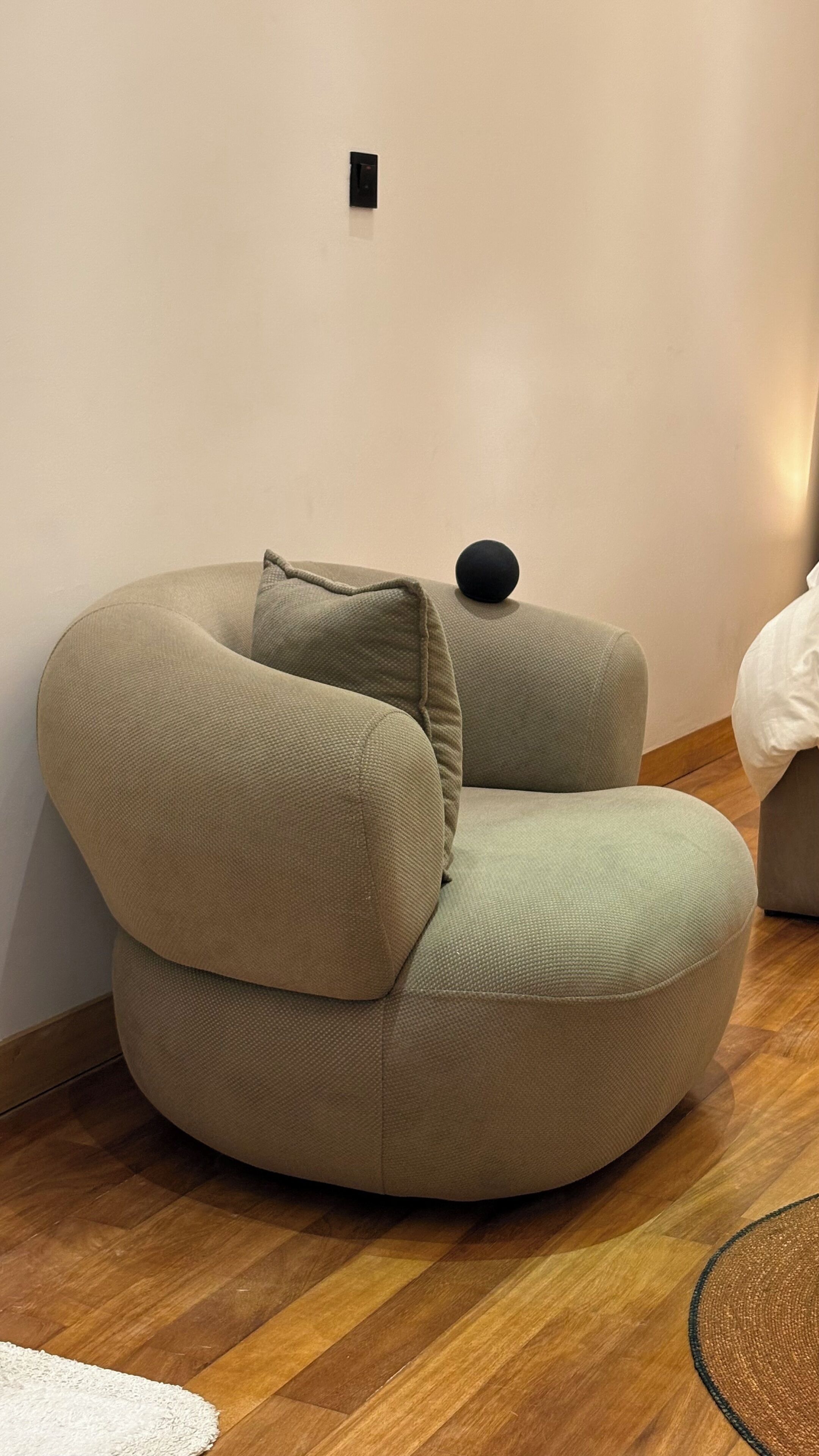 Ein modernes, gebogenes Sofa mit einer strukturierten Stoffbezug in neutraler Farbe, vor einer schlichten Wand mit Holzboden.