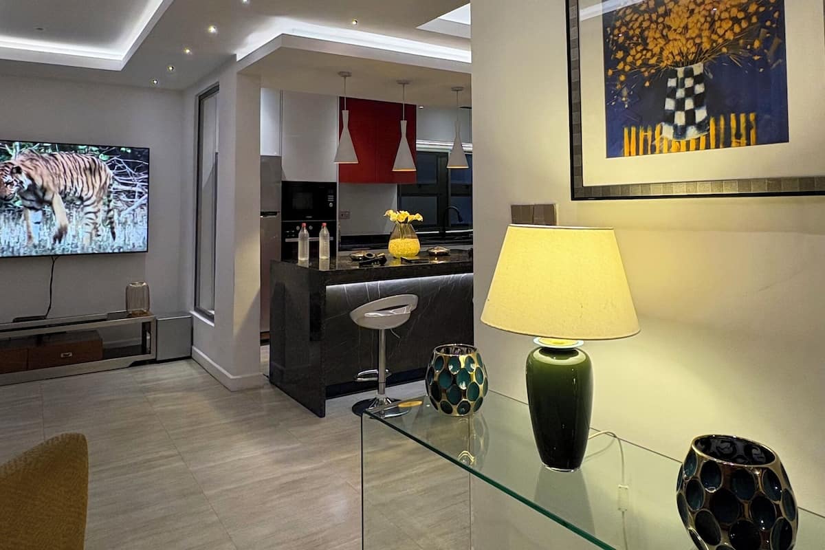 Una sala moderna con un televisor de pantalla plana, una mesa de centro de vidrio y una zona de comedor con una silla roja.
