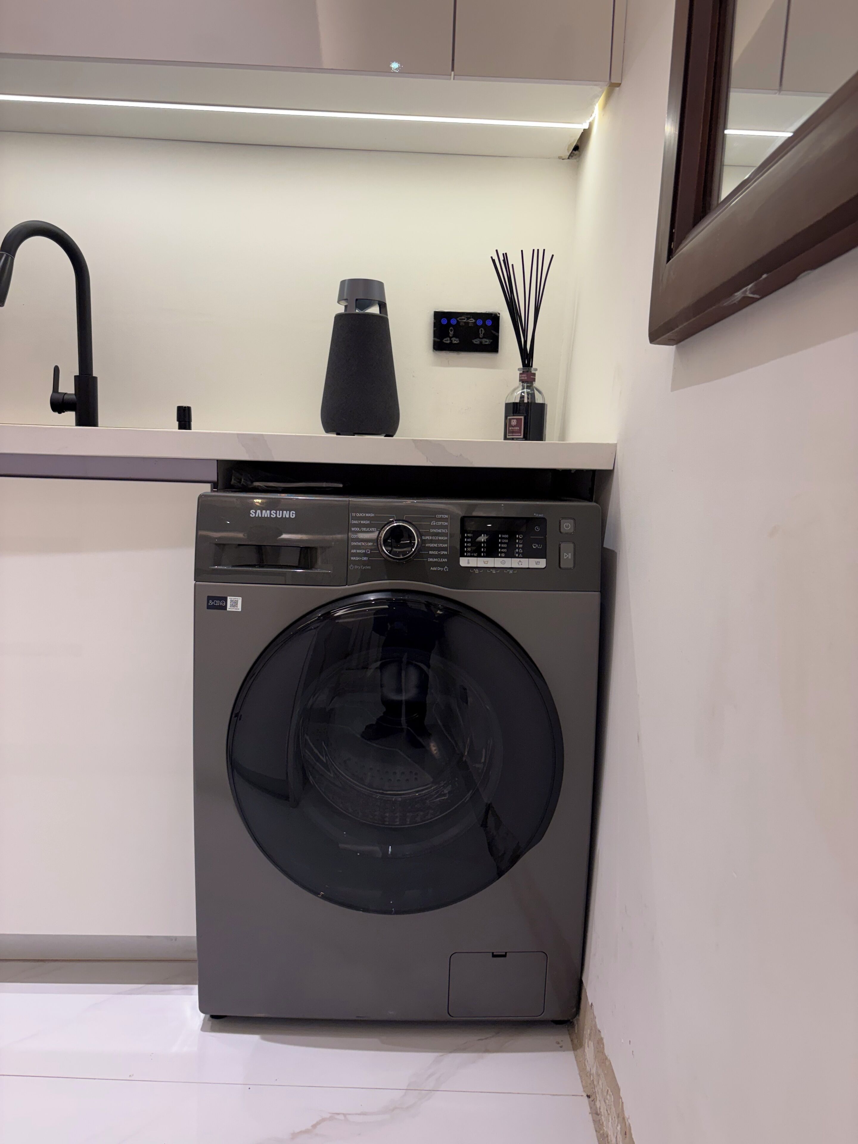 A modern kitchen with a built-in Samsung washing machine, a sleek black faucet, and a minimalist countertop design.