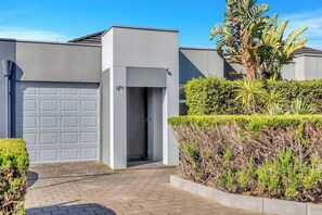 Ein modernes, zweistöckiges Haus mit Garage, überdachter Eingangspforte und einem gepflegten Garten mit verschiedenen Pflanzen.