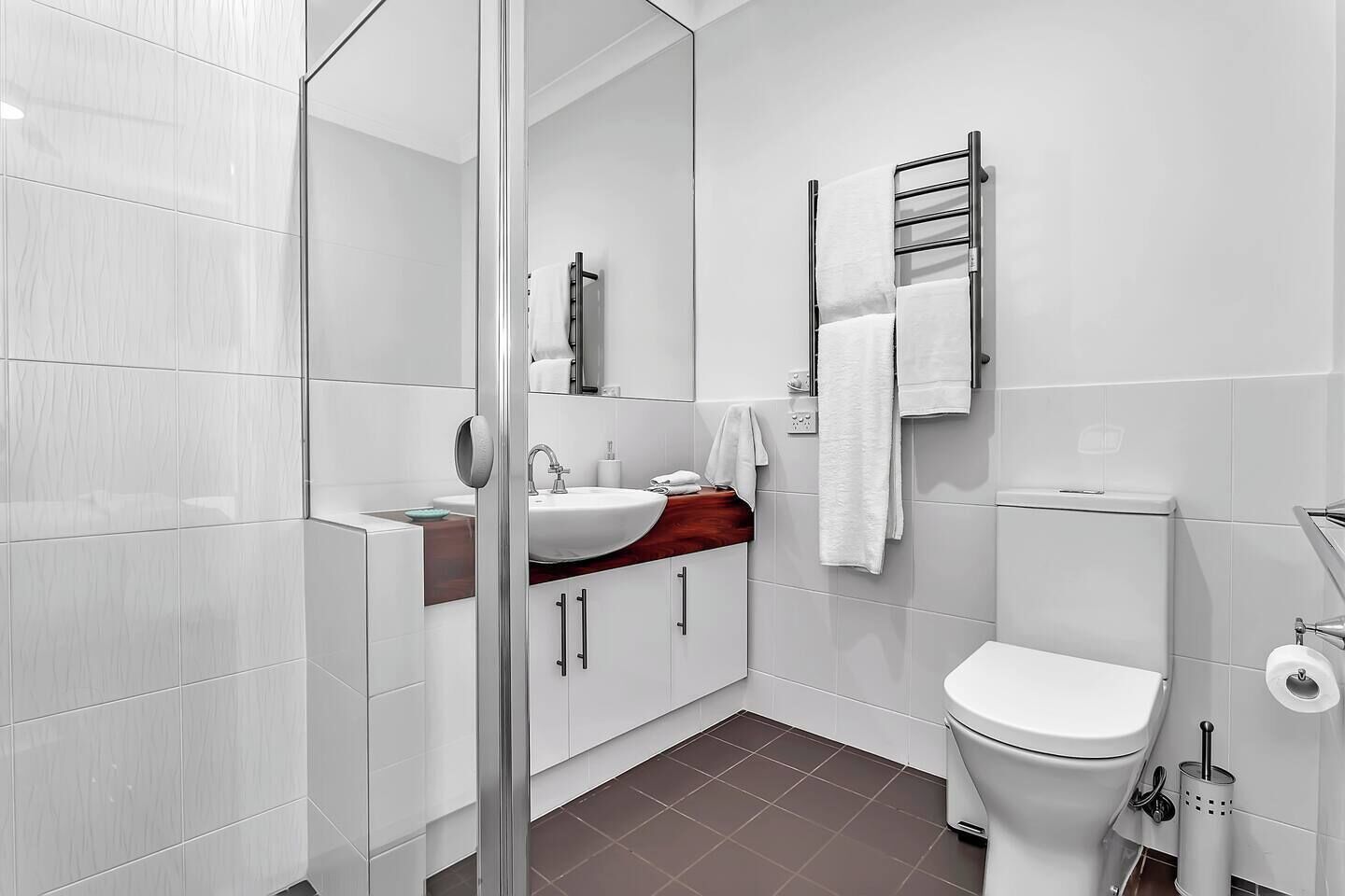 Et moderne badeværelse med en glas brusekabine, et hvidt håndvaskarrangement, en rød bordplade, et hvidt toilet og en håndklæderække.