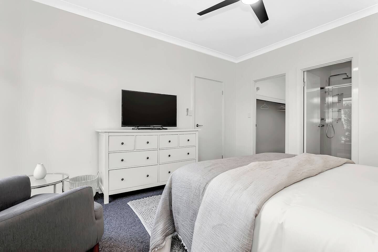 A modern hotel room with a bed, a TV on a white dresser, a desk with a chair, and a walk-in closet.