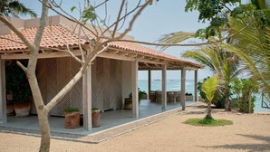 Un bâtiment situé en bord de mer, doté d’un patio couvert, de sièges en plein air et offrant une vue sur l’océan.