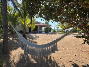A hammock in a sandy area with a building in the background. - CASA IYARI - Chamela (​Municipio de la Huerta​, Chamela)